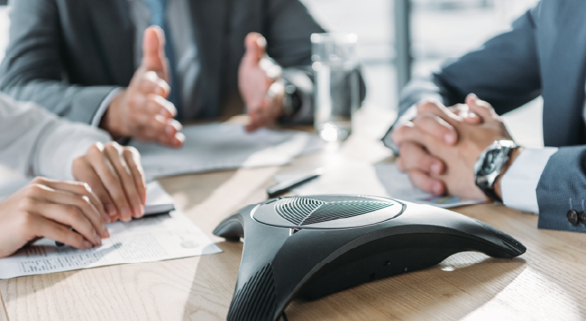 A group of business people having a conversation and using a speakerphone at an office.